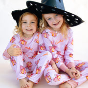 Two young girls wearing matching Halloween nightwear for kids with cartoon pumpkins and pink bows