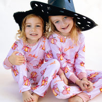 Two young girls wearing matching Halloween nightwear for kids with cartoon pumpkins and pink bows