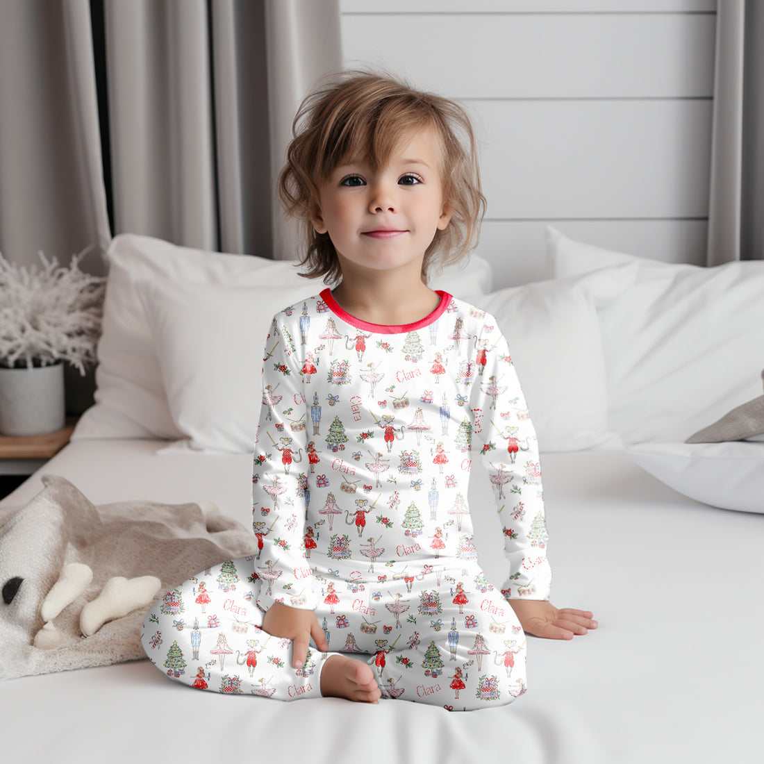 baby wearing personalized Modern Nutcracker Ballet pajamas, featuring minimalistic images from the iconic nutcracker ballet among child's name on white fabric with red cuffs.