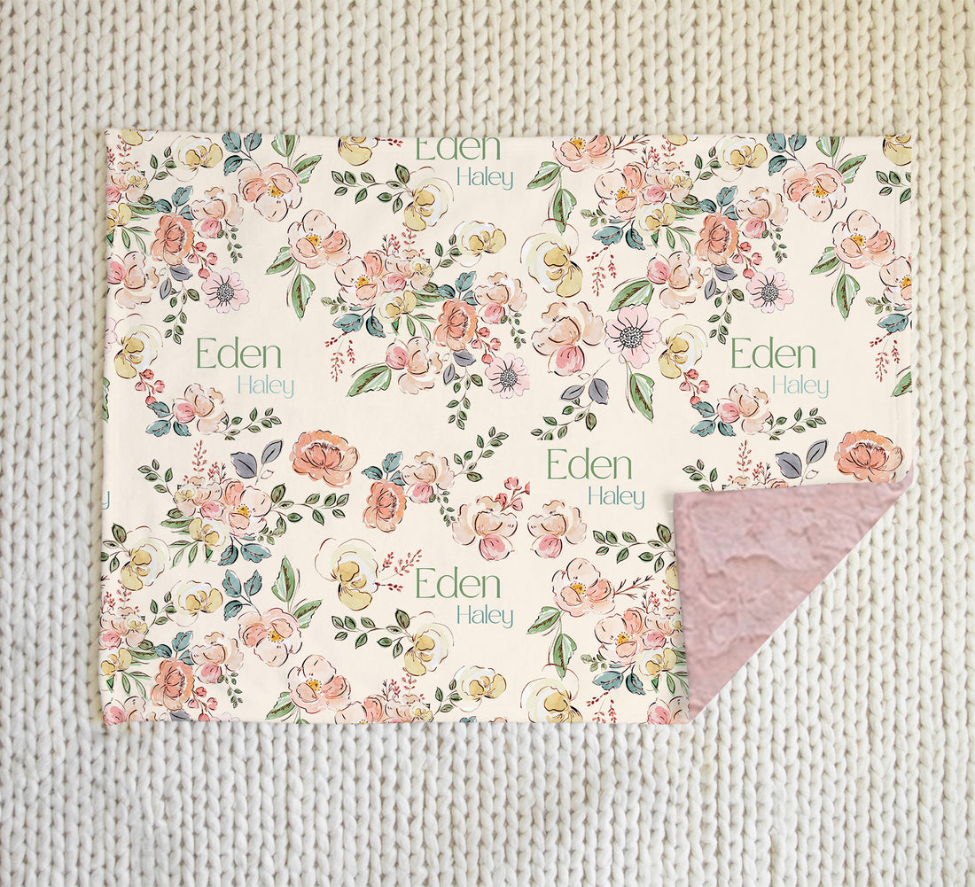 minky baby blanket with pastel colorful flowers in a sketched look with baby's name on the front side, and pink minky faux fur on the back