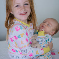 Big sister cuddling baby sibling in matching personalized pajamas with colorful letters and names, showing soft stretchy fabric and cozy comfort.