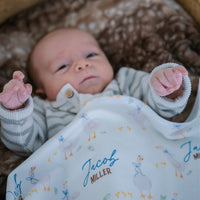 soft white baby blanket with geese and personalized name draped across baby boy in bassinet