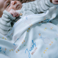 soft white baby blanket with geese and personalized name draped across baby boy in bassinet