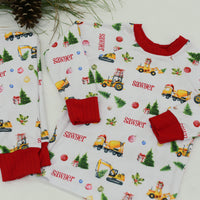 Construction Christmas Pajamas set (top and bottoms) personalized with a child's name in red font laying next to Christmas decorations.