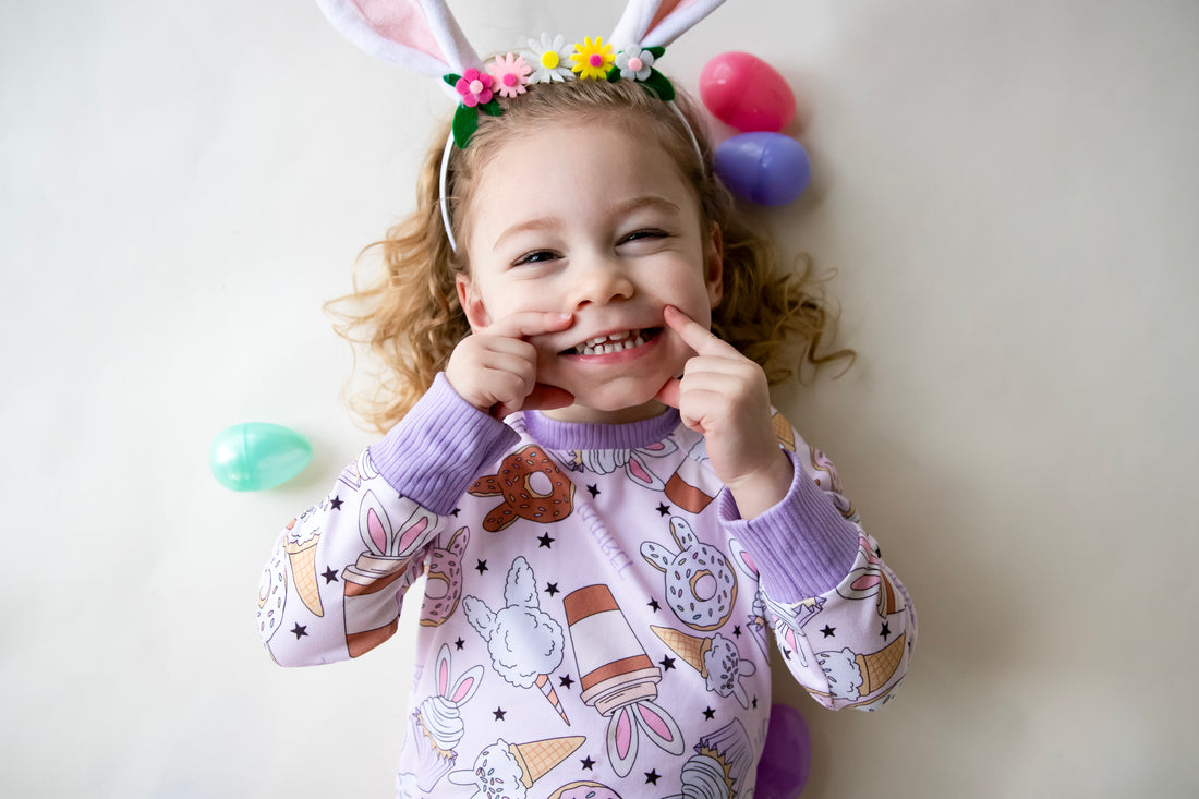 Little girl wearing cute easter sleepwear for kids, girl Easter pajamas with bunny shaped sweet treats on a lavender stretchy background.
