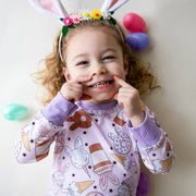 Little girl wearing cute easter sleepwear for kids, girl Easter pajamas with bunny shaped sweet treats on a lavender stretchy background.