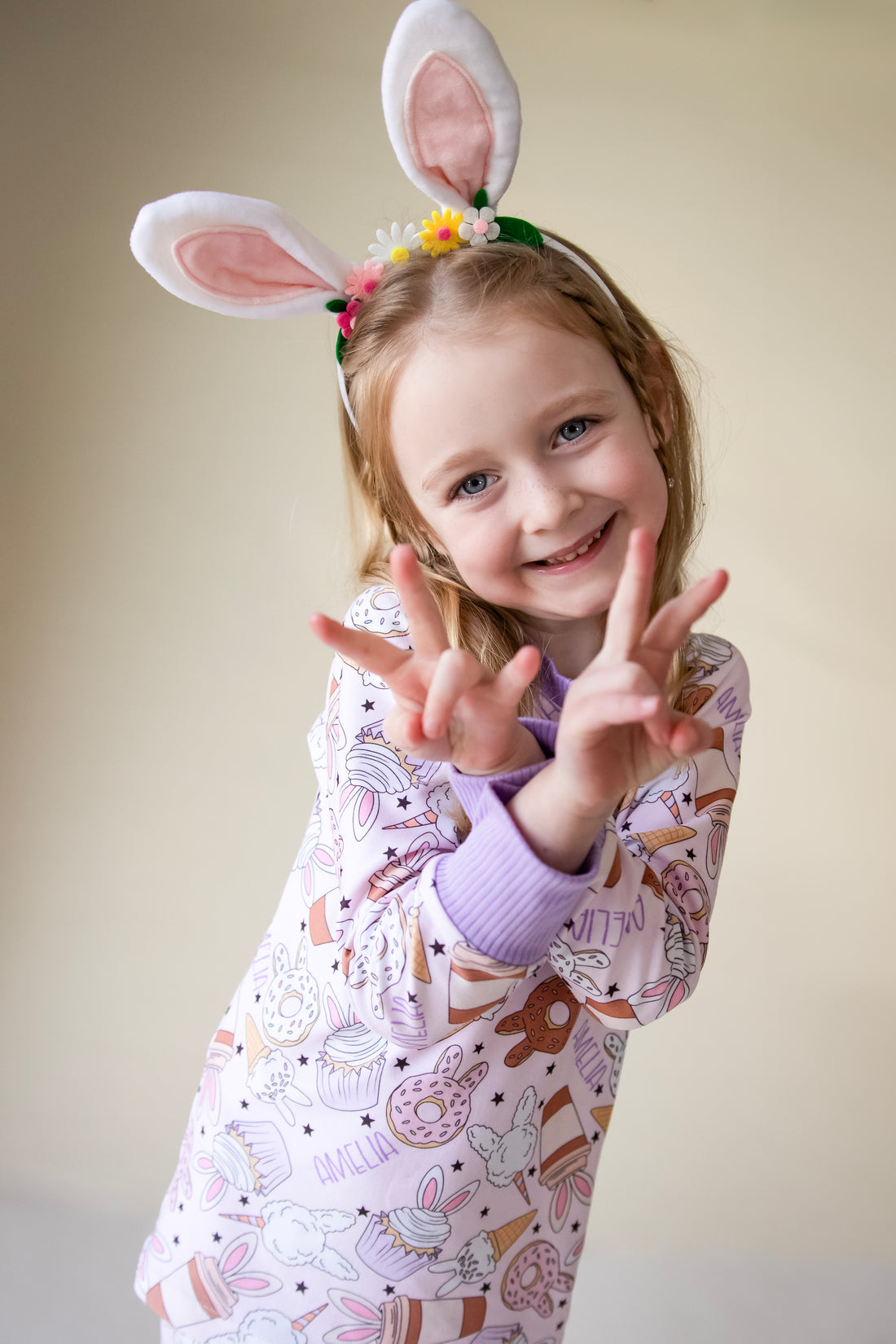 Little girl wearing cute easter sleepwear for kids, girl Easter pajamas with bunny shaped sweet treats on a lavender stretchy background.