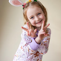 Little girl wearing cute easter sleepwear for kids, girl Easter pajamas with bunny shaped sweet treats on a lavender stretchy background.