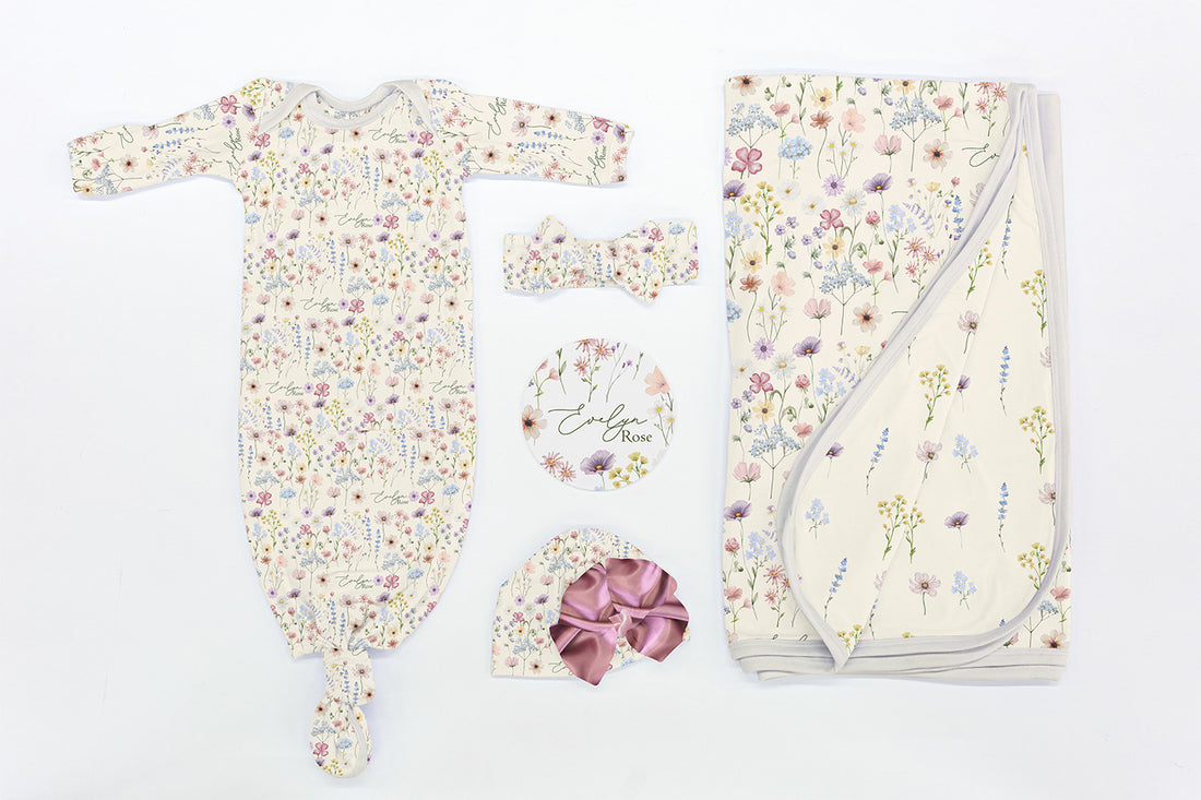 Flat lay of Wildflowers Take Me Home Set with personalized baby gown, floral blanket, bow, hat, and name disc