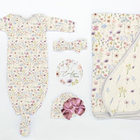 Flat lay of Wildflowers Take Me Home Set with personalized baby gown, floral blanket, bow, hat, and name disc