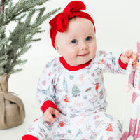 Little baby sitting by Christmas tree and wearing Nutcracker Pajamas.