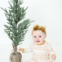 Little baby sitting in front of a Christmas tree wearing yellow striped Christmas pajamas.