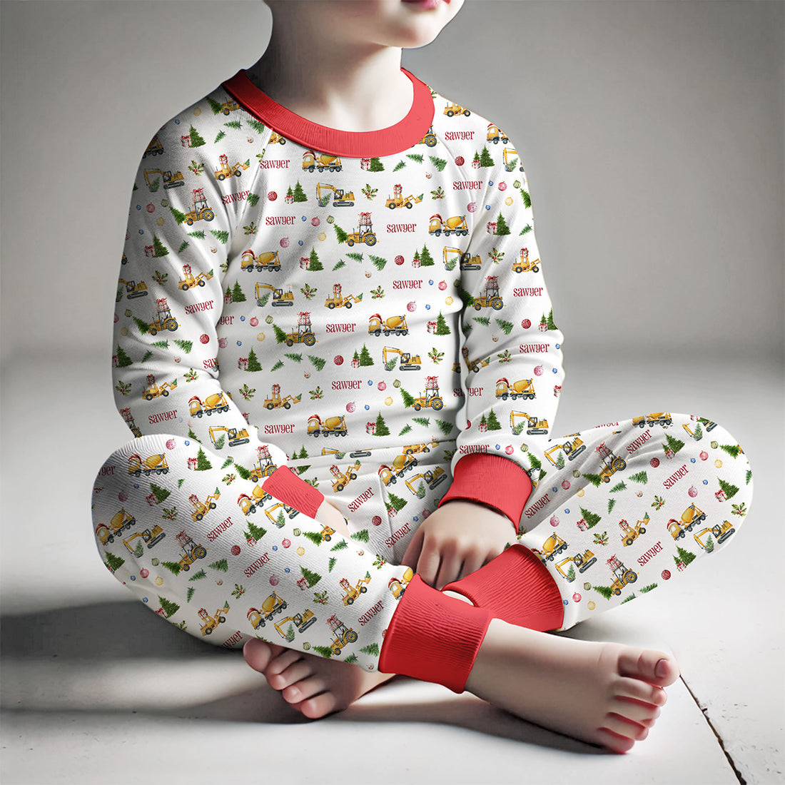 little boy wearing Construction Christmas pajamas with construction vehicles in Santa hats and Christmas trees.