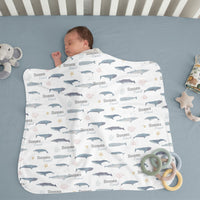 A baby is sleeping peacefully on a blue blanket with a whale and starfish pattern, surrounded by toys.