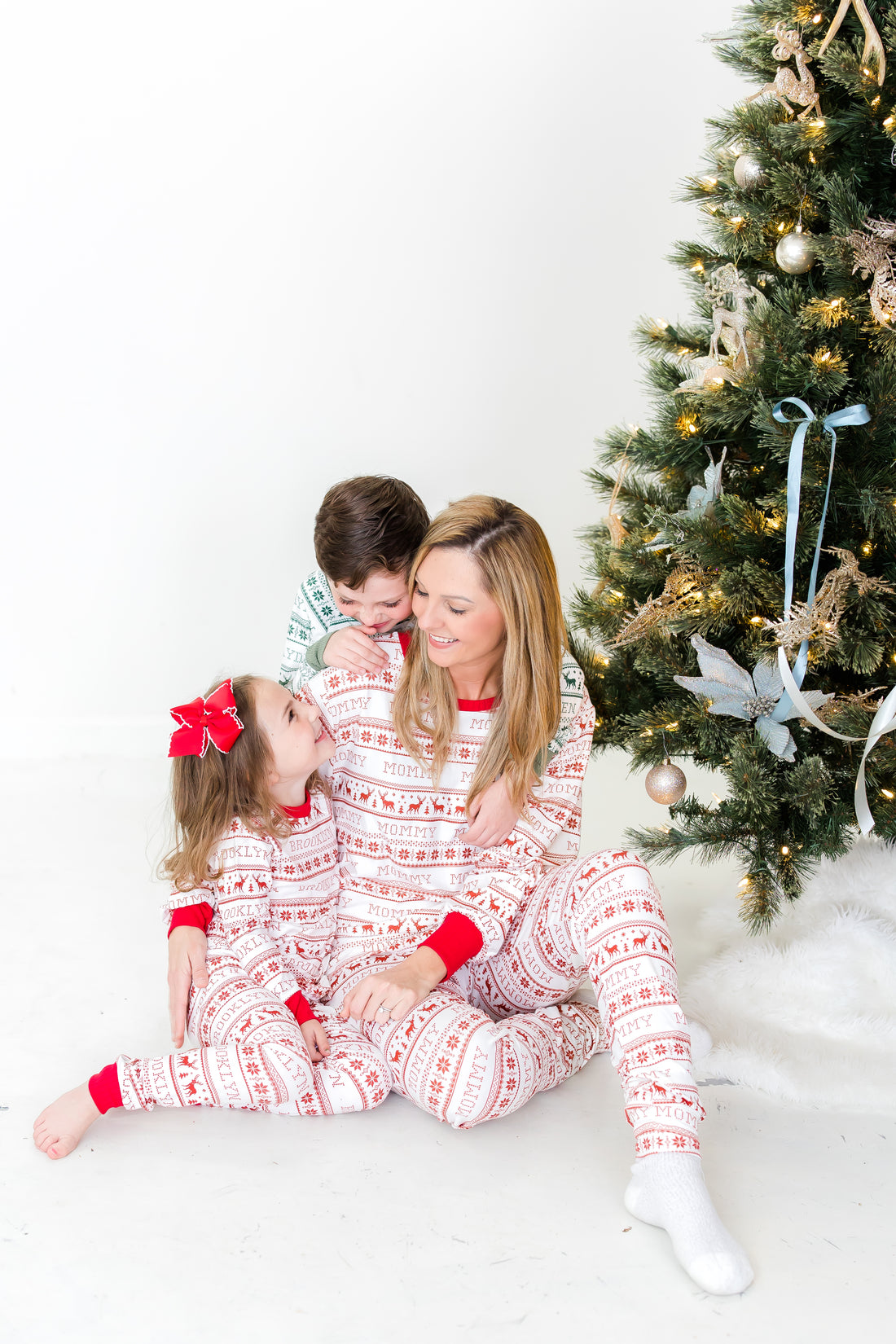 Family sitting in front of the Christmas tree wearing matching family striped Christmas pajamas.