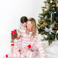 Family sitting in front of the Christmas tree wearing matching family striped Christmas pajamas.