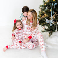 Family smiling and wearing matching striped Christmas pajamas in front of Christmas tree.