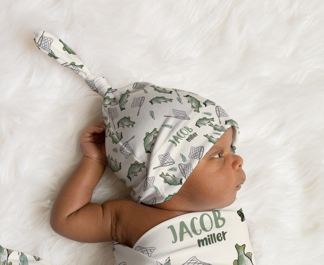 Baby wearing a fishing-patterned hat and matching swaddle with name