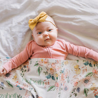 Baby lying on a floral blanket with a pink outfit and yellow headband.