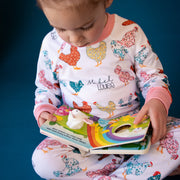 little girl wearing personalized chicken pajamas with a calico design in various colors, her name in script font on a white knit background, and pink cuffs.