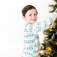 Young boy wearing green striped Christmas Pajamas and hanging ornaments on Christmas tree.