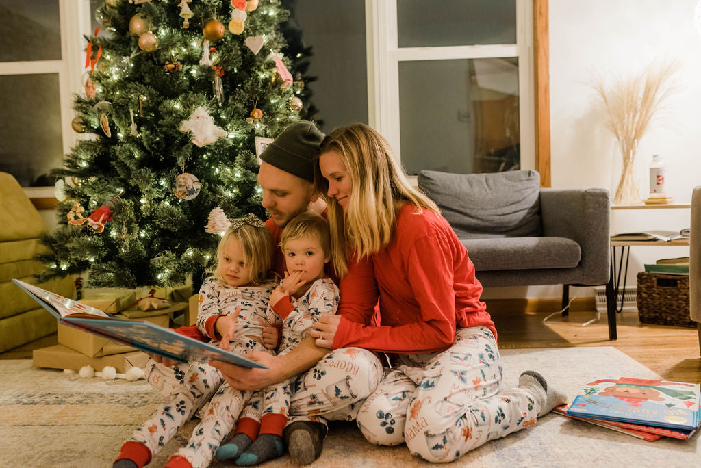 Mom, Dad, and children all wearing hot cocoa matching Christmas Pajamas in front of Christmas tree.