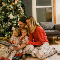 Mom, Dad, and children all wearing hot cocoa matching Christmas Pajamas in front of Christmas tree.