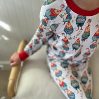 Little girl wearing personalized festive chickens christmas pajamas that feature cute chickens wearing sweaters and scarves on a white background and red cuffs.