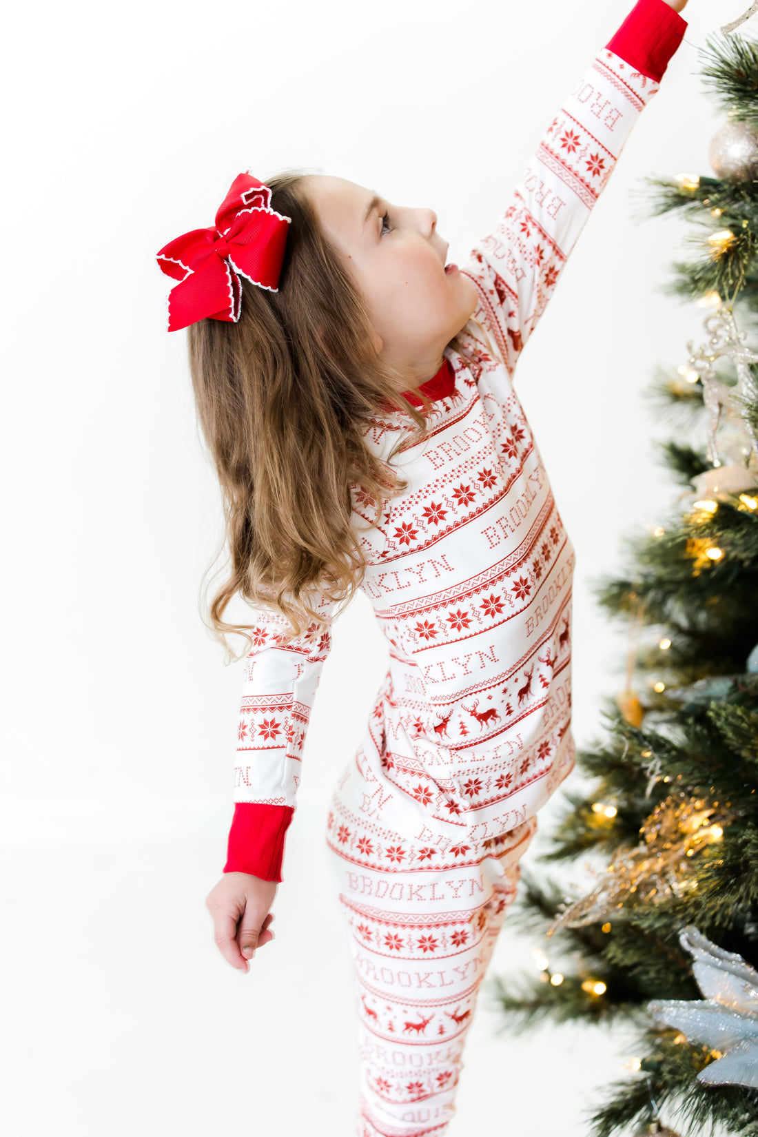 Young girl wearing red striped Christmas pajamas near a Christmas tree.