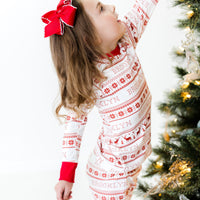 Young girl wearing red striped Christmas pajamas near a Christmas tree.