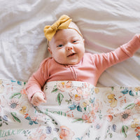 Baby lying on a floral blanket wearing a pink outfit and yellow headband.