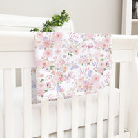 A white crib with a floral print blanket hanging from the rail.