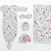 Baby clothing set with onesie, hat, and blanket featuring geese and floral and bow designs on a white background.