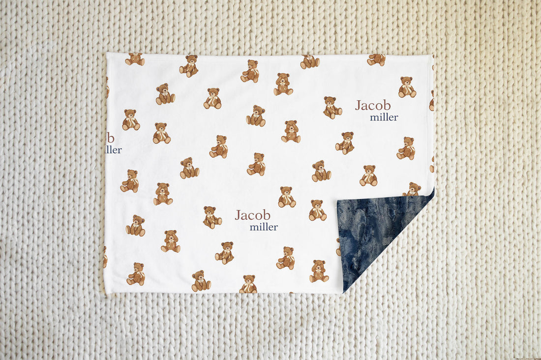 white minky baby blaket with brown teddy bears and baby's name in text on the front, and navy blue minky plush fur on the back