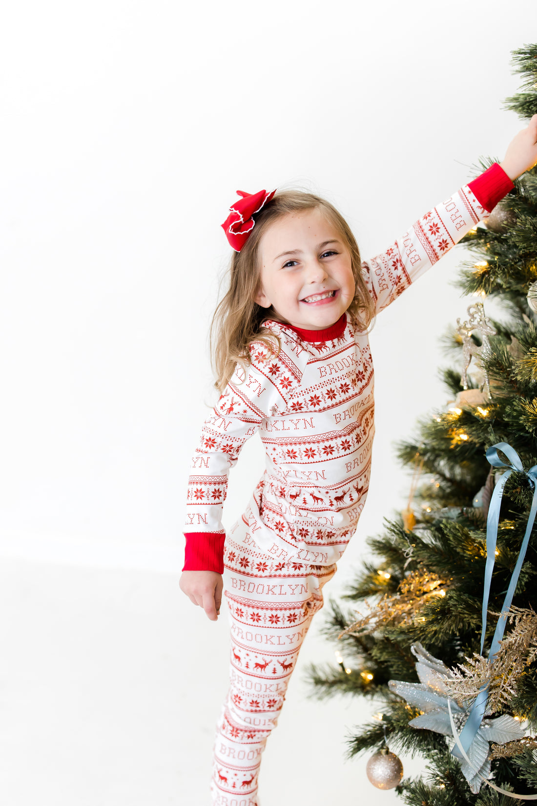 Young girl wearing red striped Christmas Pajamas and hanging ornaments on Christmas tree.