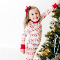 Young girl wearing red striped Christmas Pajamas and hanging ornaments on Christmas tree.