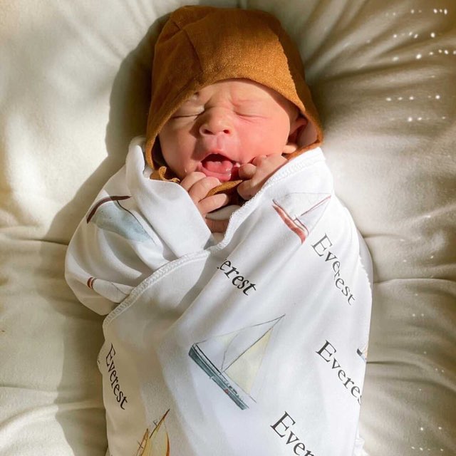 Baby laying down wrapped up in their personalized sailboat swaddle blanket.