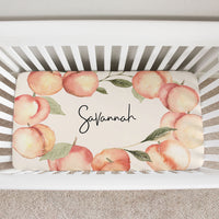 top view of a custom crib sheet. It has a frame of big watercolor peaches for the Georgia Peach in your life. Her name is written in the middle with a modern font.