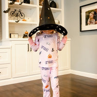 Child in pink Halloween pajamas with name and pumpkin prints, wearing a black witch's hat.