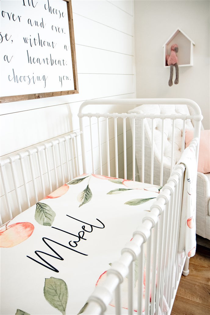 White iron bed in newborn nursery with an ivory custom crib sheet for baby bedding. Personalized with name of child in middle