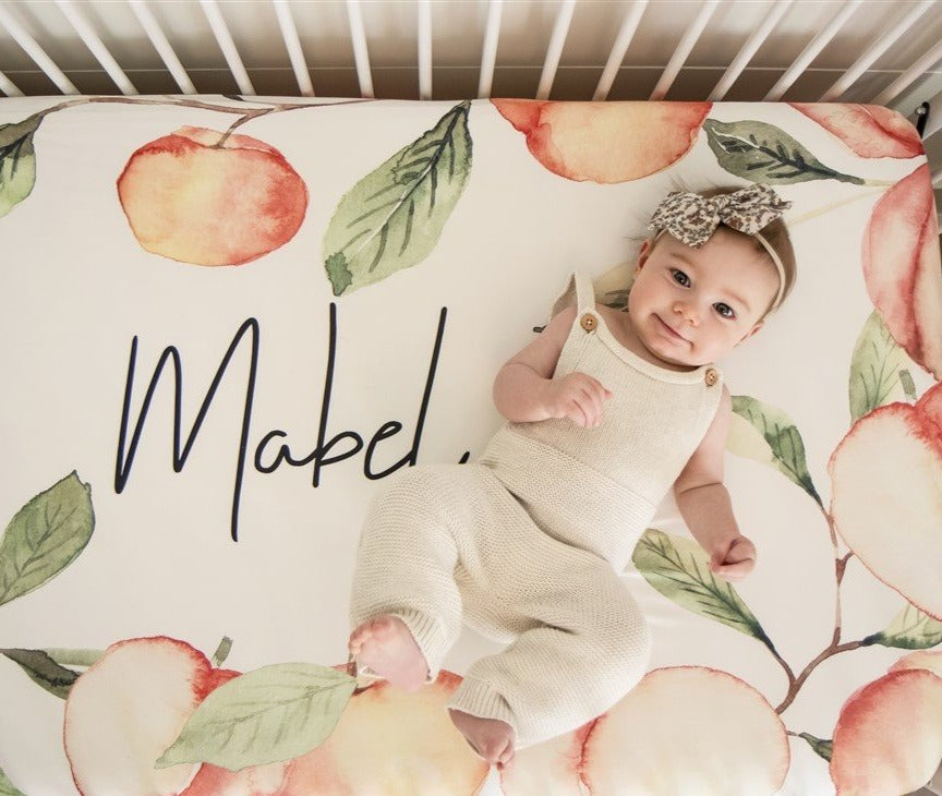Custom Crib Sheet with a peach design for a baby girl nursery. Natural watercolor peaches on ivory background fabric with name printed in the middle.