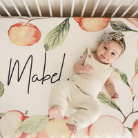 Custom Crib Sheet with a peach design for a baby girl nursery. Natural watercolor peaches on ivory background fabric with name printed in the middle.