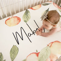 personalized crib sheet for a baby with watercolor peaches on it and the name of baby written in the middle of a peach frame that reaches all around the edges of custom crib sheet
