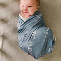 A baby laying in a bassinet swaddled in a personalized stretchy swaddle blanket.