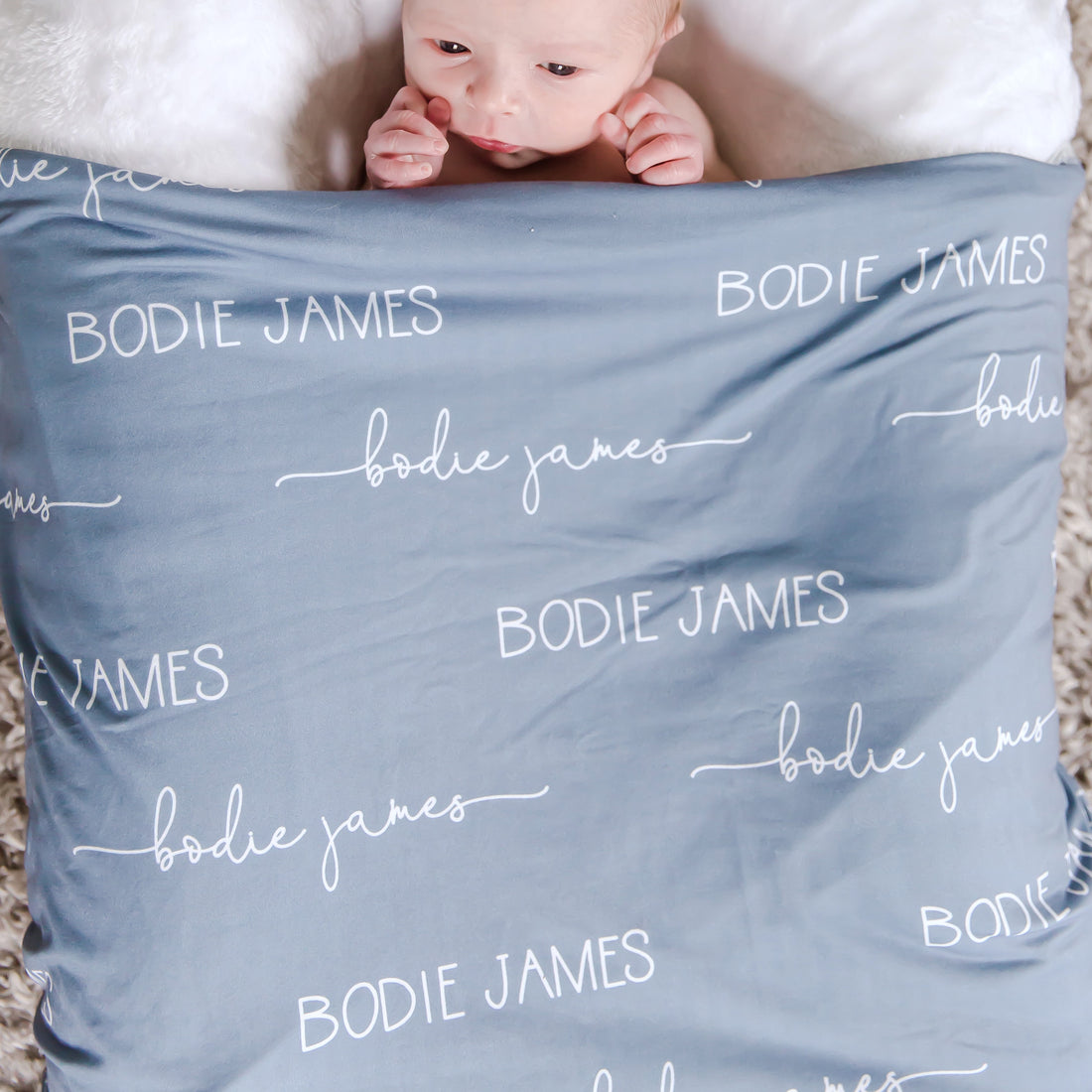 A baby laying with their personalized stretchy blue swaddle blanket.