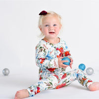 Little girl sitting and smiling while wearing floral Christmas pajamas with red, white and blue flowers.