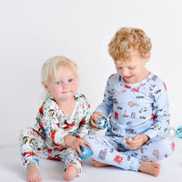 Young girl wearing Floral Christmas Pajamas with bouquets of red, white, and light blue flowers and holly leaves, and playing with her brother who is wearing Christmas pajamas.