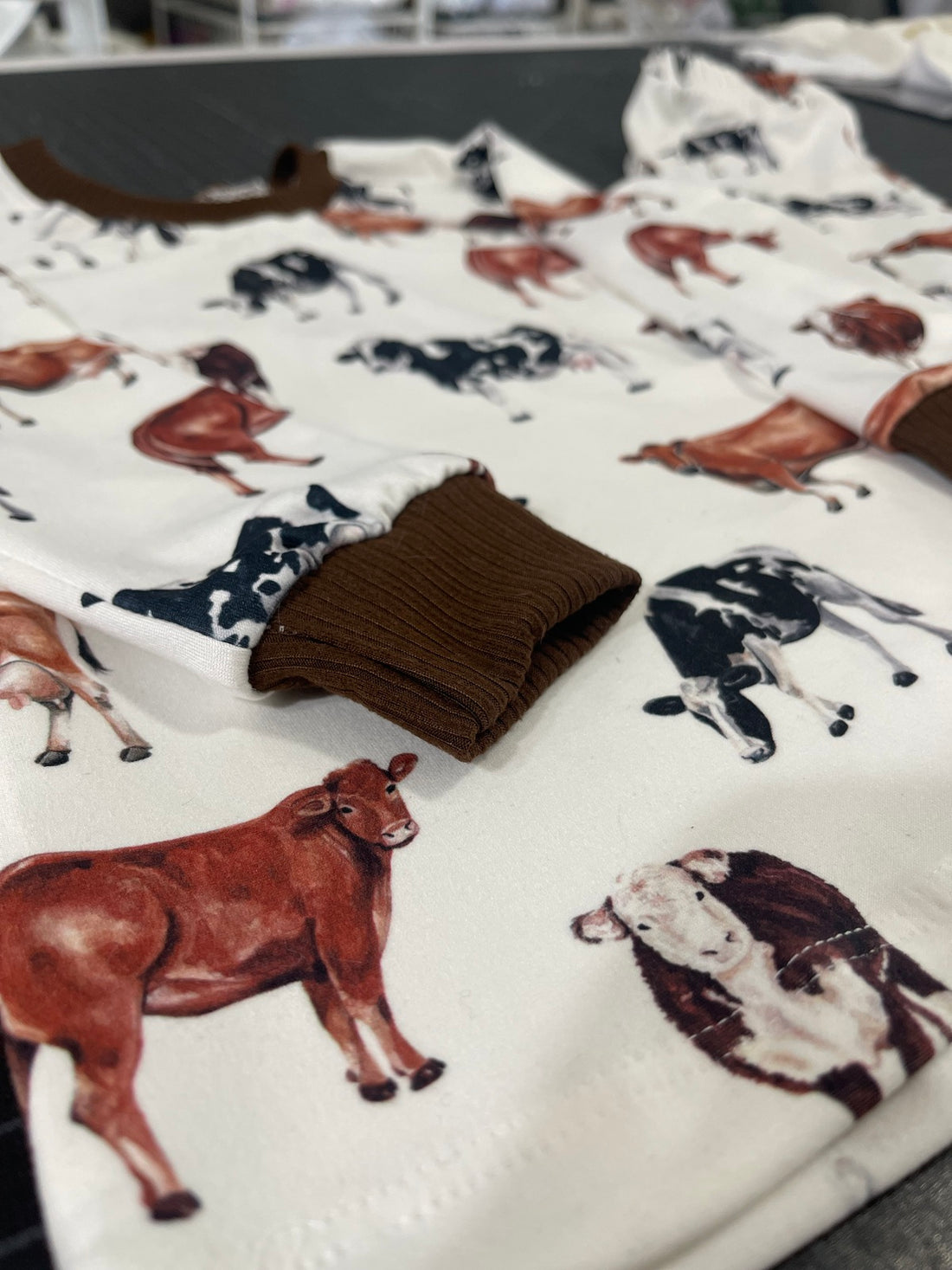 Close up view of our personalized cow pajamas. The pajamas have brown, black, and white cows on the shirt and pants. The cuffs on the shirt and pants are brown to match the design.