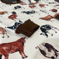 Close up view of our personalized cow pajamas. The pajamas have brown, black, and white cows on the shirt and pants. The cuffs on the shirt and pants are brown to match the design.