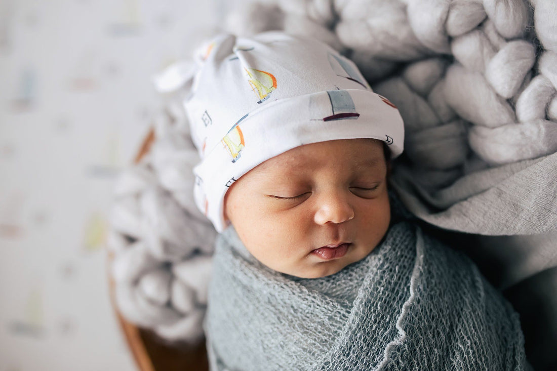 Baby sleeping in their stretchy boat swaddle with a matching sailboat hat.